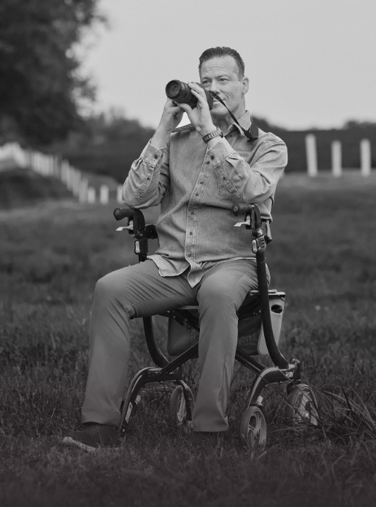 Ambassador Scott, who has LOPD, sitting in a wheelchair while taking a photo with his digital camera